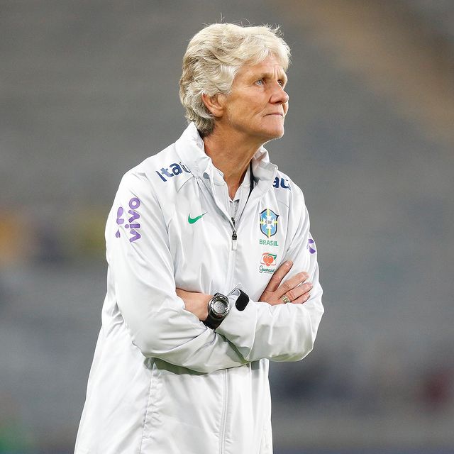 A treinadora Pia Sundhage da Seleção Brasileira feminina, com os braços cruzados e uniforme branco, observa algo durante um treino