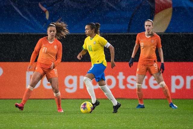 Marta, com o uniforme da Seleção Brasileira, domina a bola em campo enquanto é observada por duas jogadoras da Holanda