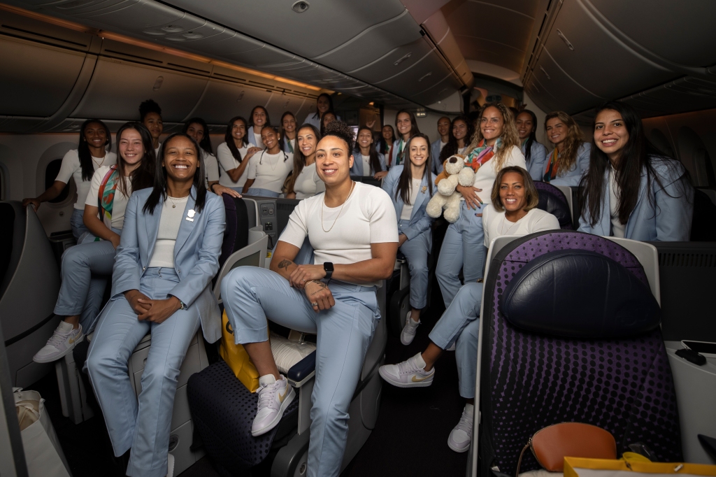 Jogadoras da Seleção Brasileira feminina, com trajes que misturam branco e cinza, posam dentro do avião no qual viajaram para disputar a Copa do Mundo 2023
