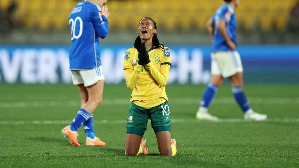 Ajoelhada no chão, Linda Motlhalo, camisa 10 da África do Sul, comemora a vitória sobre a Itália. Ao fundo, duas jogadoras italianas lamentam a derrota