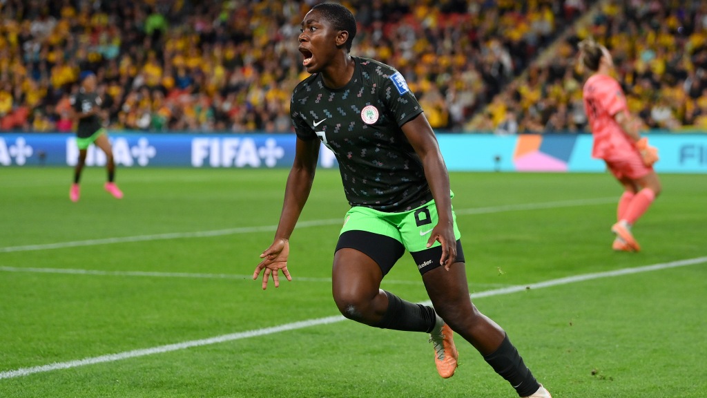 Asisat Oshoala, vestindo uniforme de camisa preta e calção verde claro, corre para comemorar um gol marcado na Copa do Mundo feminina pela Nigéria